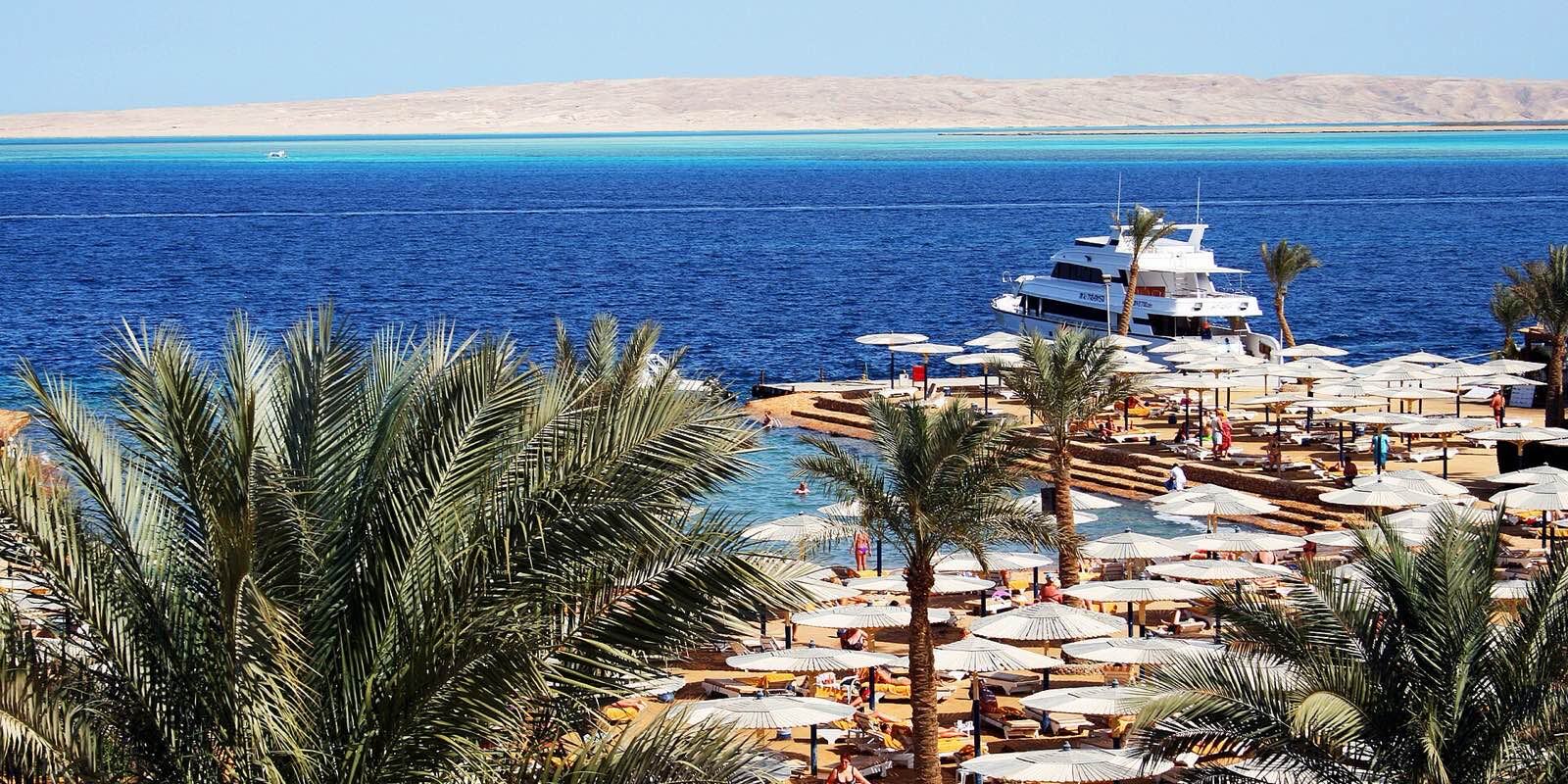 Palmer og båt ved en hotellstrand i Hurghada med Rødehavet og ørkenfjell