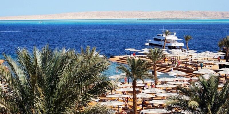 Palmer og båt ved en hotellstrand i Hurghada med Rødehavet og ørkenfjell